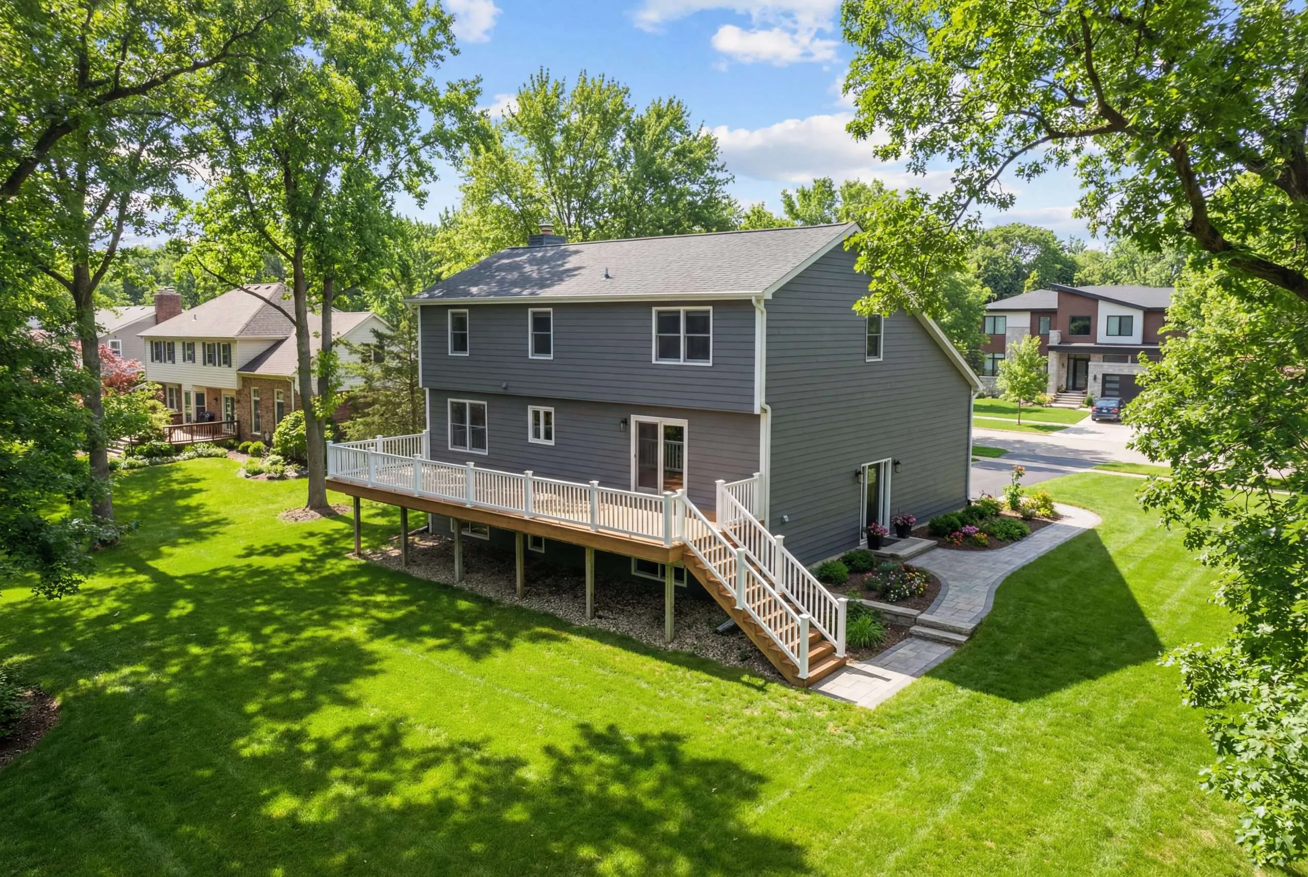 A majestic suburban house facade features a charming walkout deck with pristine white railings and inviting stairs overlooking the lawn